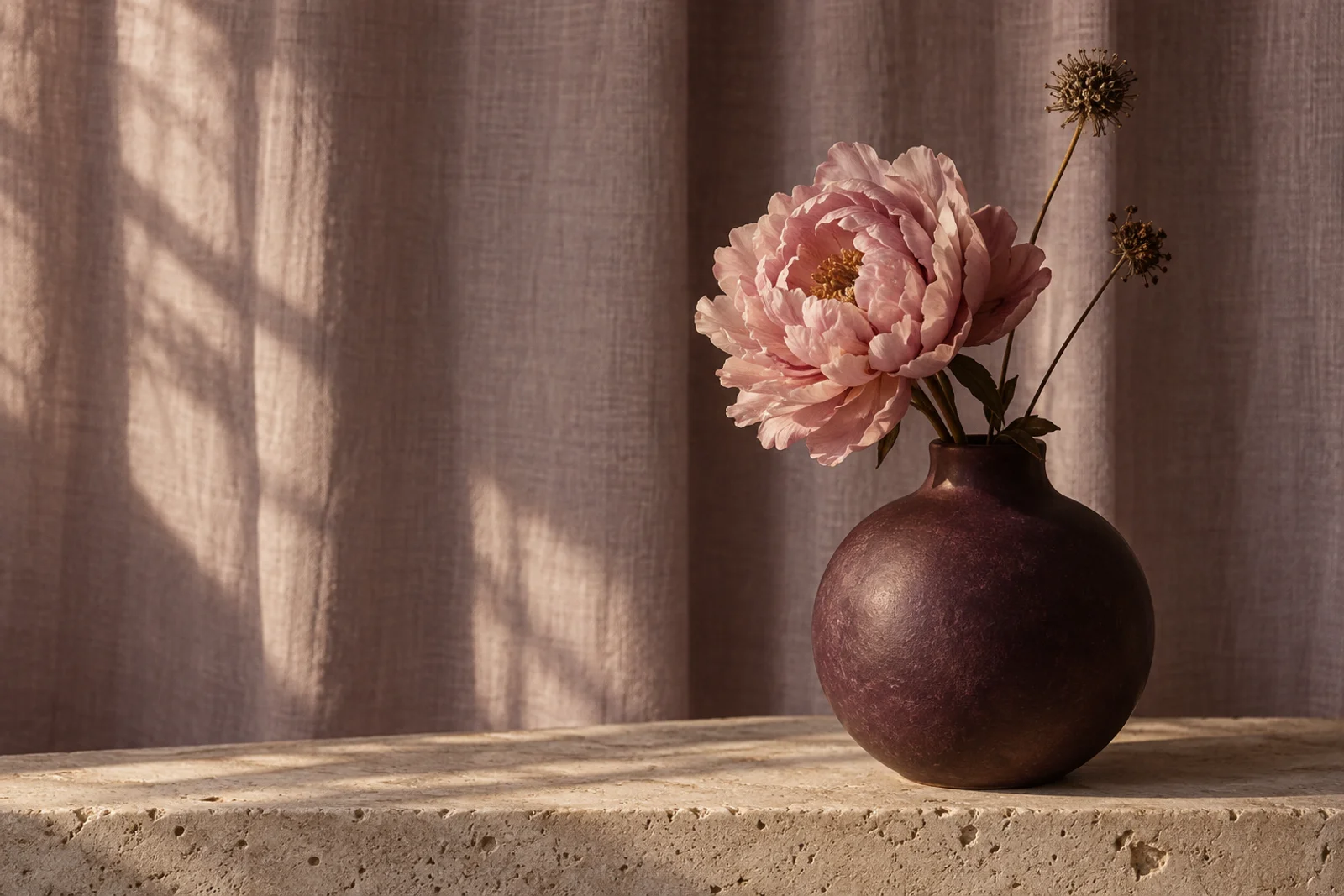 A pink peony in a plum ceramic vase, with warm light on a linen curtain